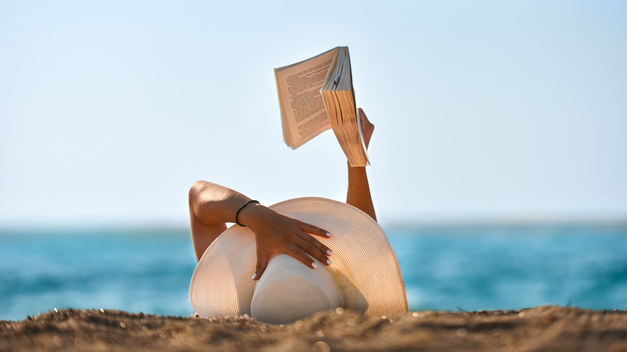 Foto de archivo de una joven leyendo un libro en la playa