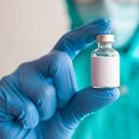 A female healthcare worker in vibrant colored protective suit is holding a medicine vial
