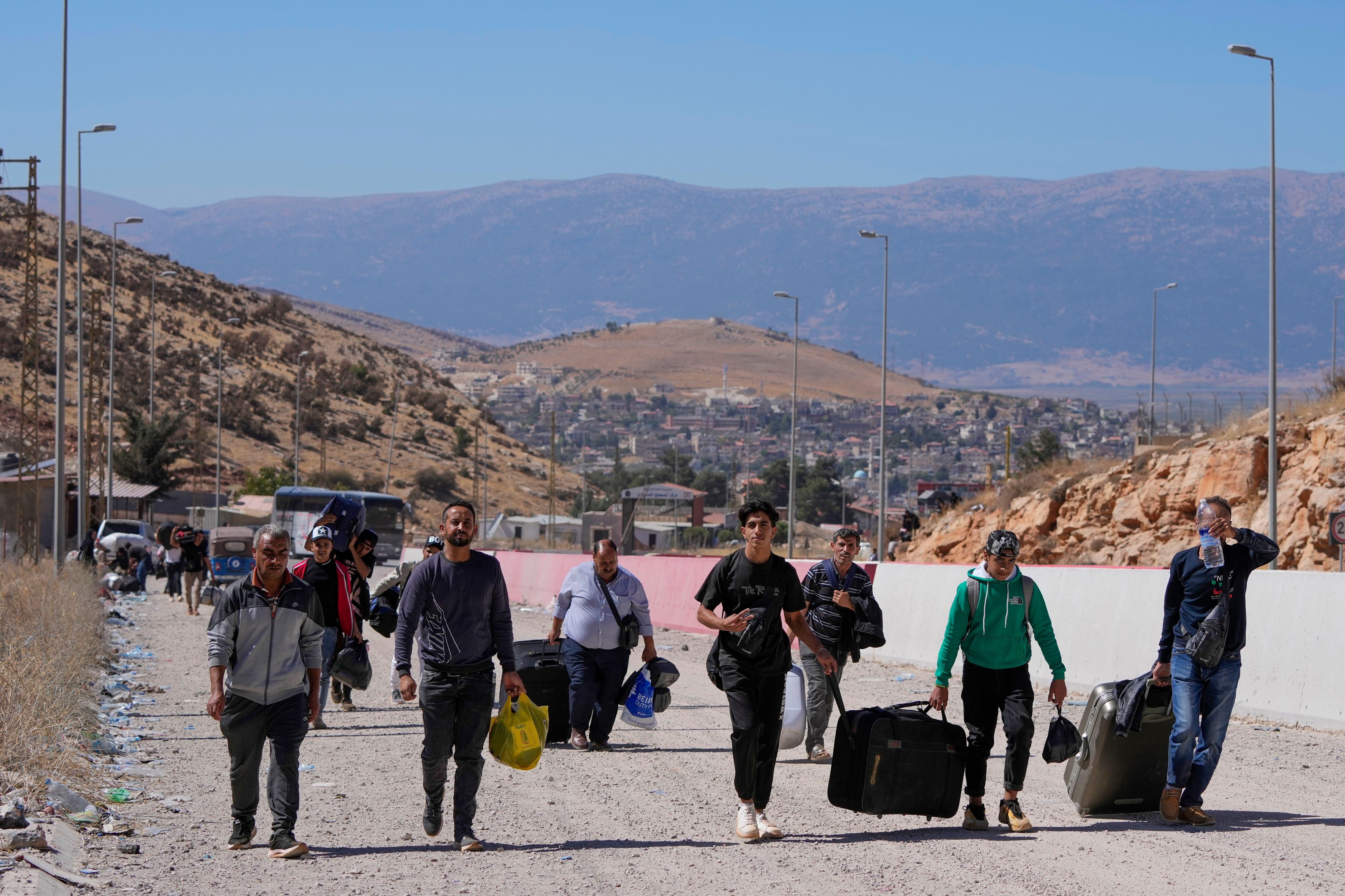 La gente carga su equipaje mientras cruza a pie a Siria, a través de un cráter causado por los ataques aéreos israelíes que tenían como objetivo bloquear la carretera Beirut-Damasco en el cruce de Masnaa, en el valle oriental de Bekaa, Líbano, el sábado 5 de octubre de 2024. (Foto AP /Hassan Ammar)