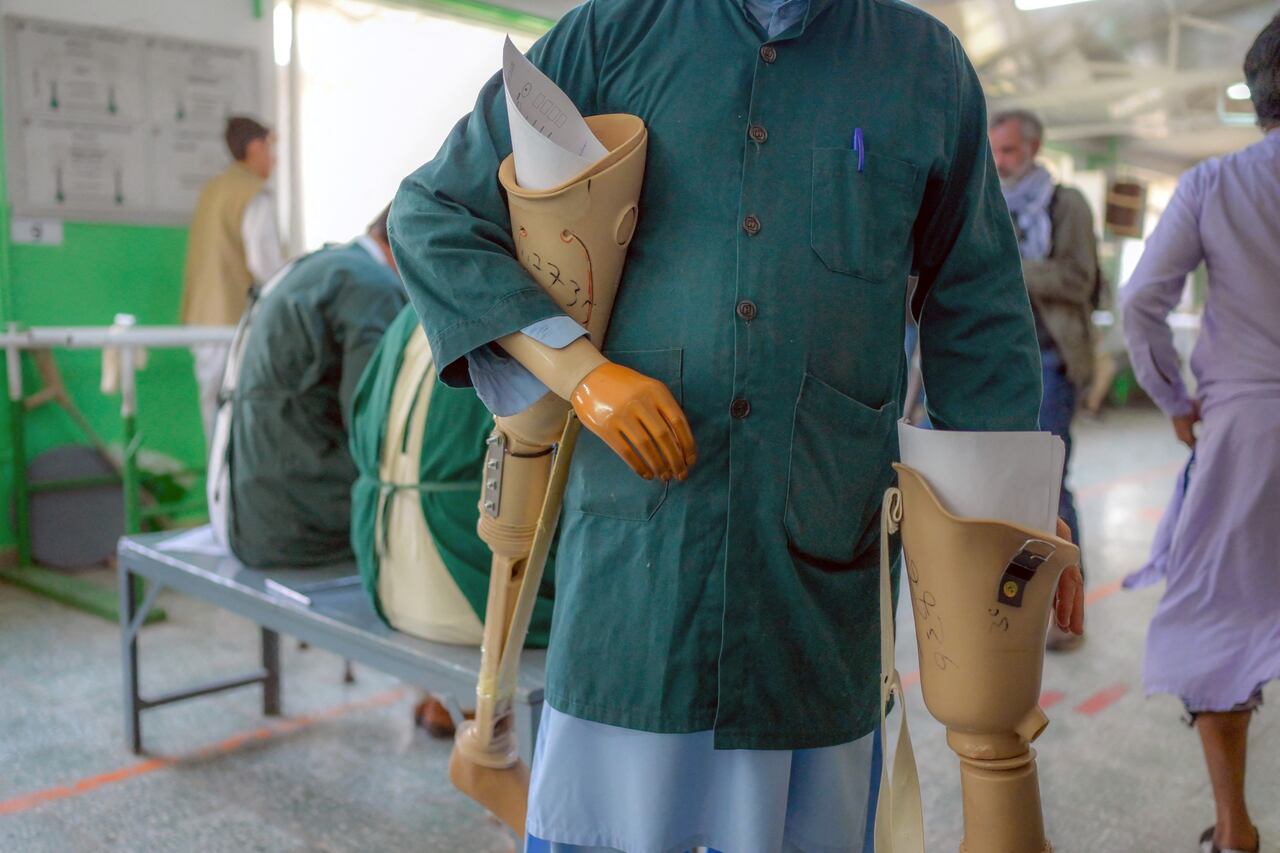 In this photograph taken on October 11, 2021, a worker with a prosthetic arm carries prosthetic legs at the International Committee of Red Cross Rehabilitation Centre in Kabul. - Just months ago they were fighting each other as mortal enemies, but today they are amputees dealing with their new disability, together. At this Red Cross-run rehabilitation centre in Kabul, former Afghan government soldiers and Taliban fighters adjust their new prostheses, living side by side. (Photo by BULENT KILIC / AFP) / TO GO WITH: Afghanistan-conflict-health-disability, FOCUS by Emmanuel Peuchot