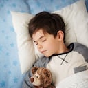Niño de seis años durmiendo en la cama en la almohada con reloj despertador y un oso de peluche.