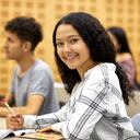 Retrato de estudiante universitario sonriente escribiendo en papel sobre la mesa. La mujer se está concentrando en el aula. Ella está en ropa informal.