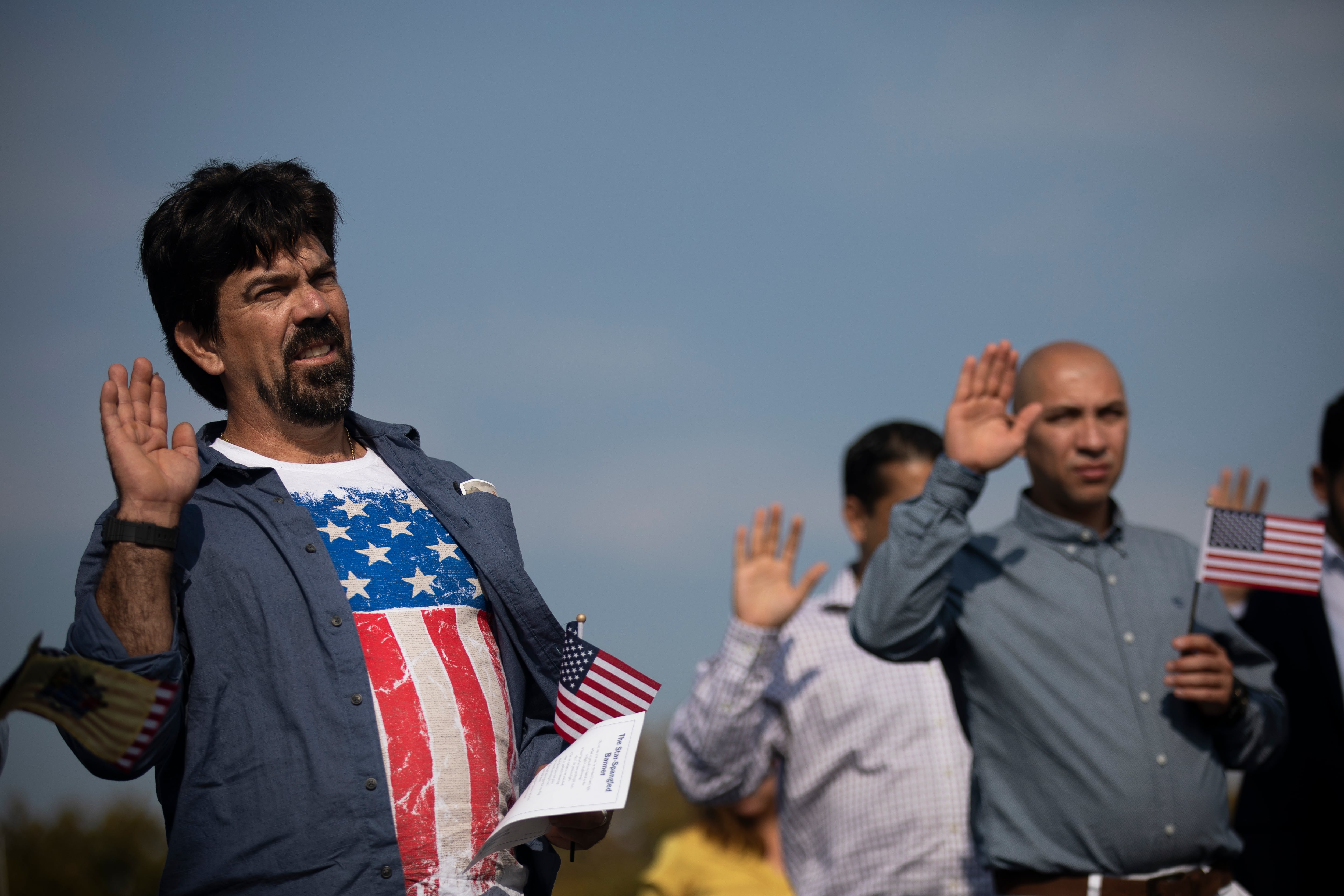 Erandy Delgobo Da Silva (L), originario de Brasil, usa una camiseta con la bandera estadounidense mientras toma el juramento de ciudadanía durante una ceremonia de naturalización en Liberty State Park