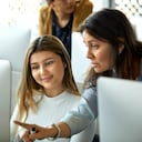 Profesor explicando estudiante en el aula. Mujer sonriente mirando PC de escritorio. Están en el laboratorio de computación.