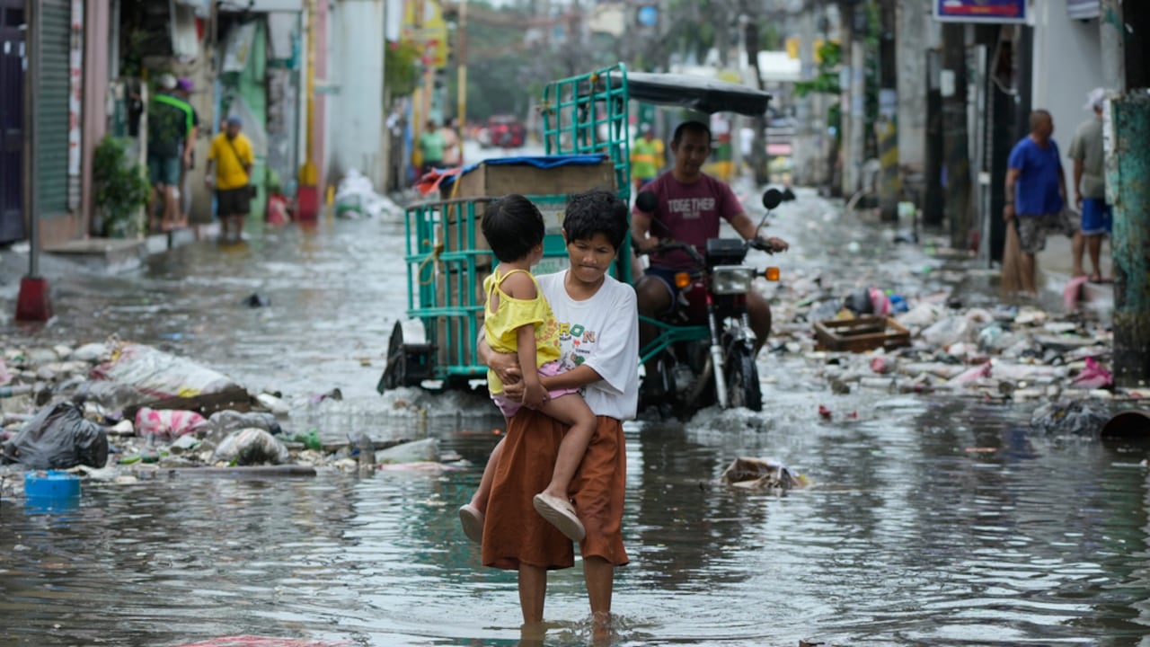 Una mujer y una niña cruzan una calle inundada debido al tifón Fung-wong y la subida de la marea el lunes 10 de noviembre de 2025, en Navotas, Filipinas. (AP Foto/Aaron Favila)