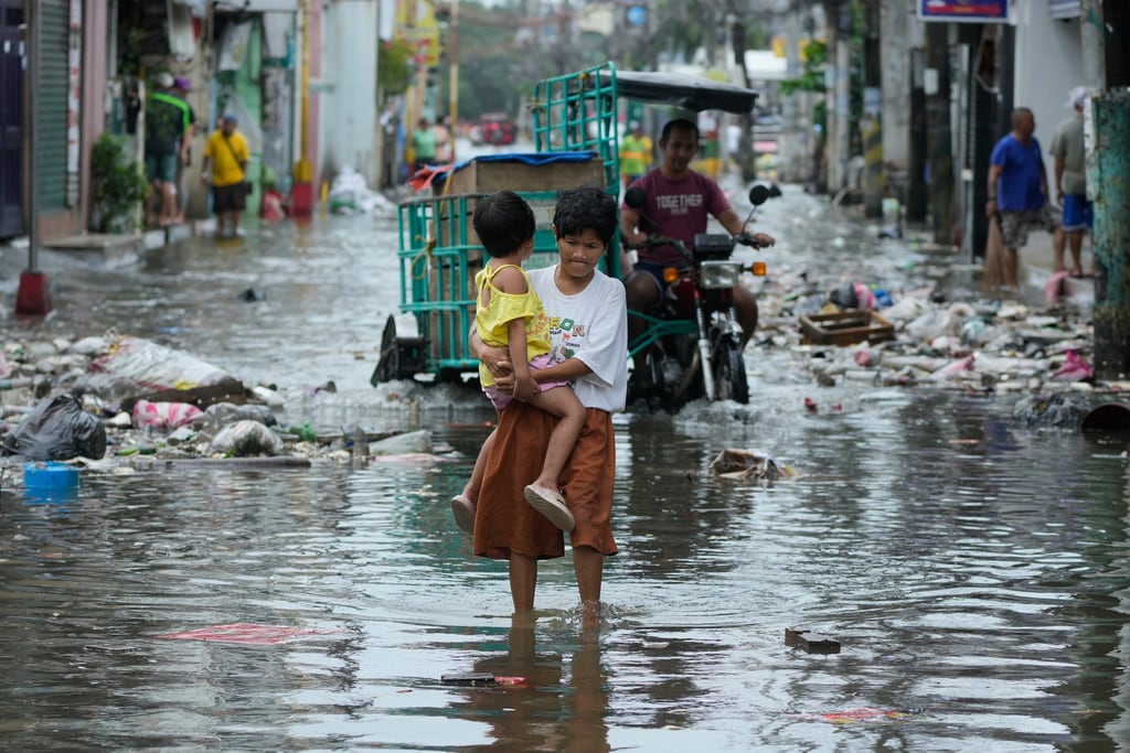 Una mujer y una niña cruzan una calle inundada debido al tifón Fung-wong y la subida de la marea el lunes 10 de noviembre de 2025, en Navotas, Filipinas. (AP Foto/Aaron Favila)