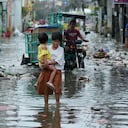 Una mujer y una niña cruzan una calle inundada debido al tifón Fung-wong y la subida de la marea el lunes 10 de noviembre de 2025, en Navotas, Filipinas. (AP Foto/Aaron Favila)
