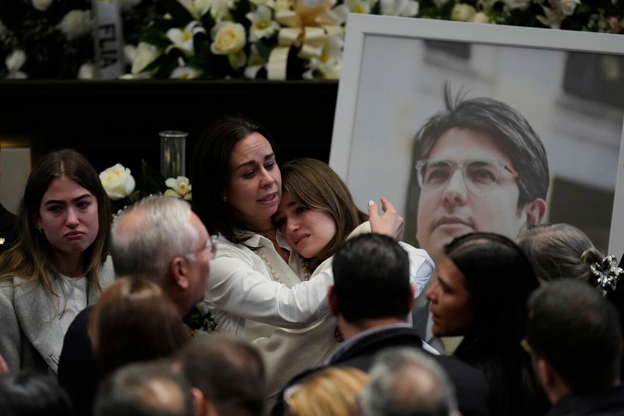 Claudia Tarazona, esposa del aspirante presidencial y senador de la oposición. Miguel Uribe, abraza a una de sus hijas junto a una foto de su marido durante una ceremonia en su honor en el Congreso de Bogotá, Colombia, el lunes 11 de agosto de 2025. Uribe murió a causa de las heridas sufridas después de que le dispararan en un mitin político. (AP Photo/Fernando Vergara)