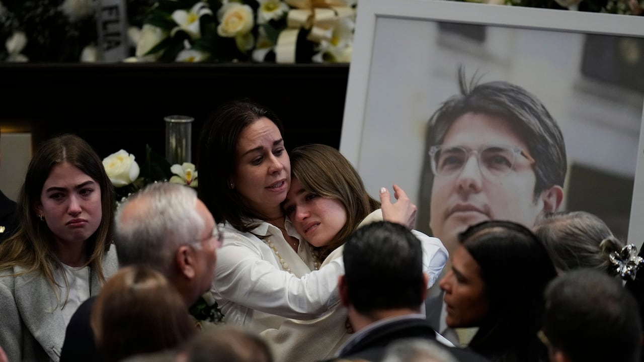Claudia Tarazona, esposa del aspirante presidencial y senador de la oposición. Miguel Uribe, abraza a una de sus hijas junto a una foto de su marido durante una ceremonia en su honor en el Congreso.
