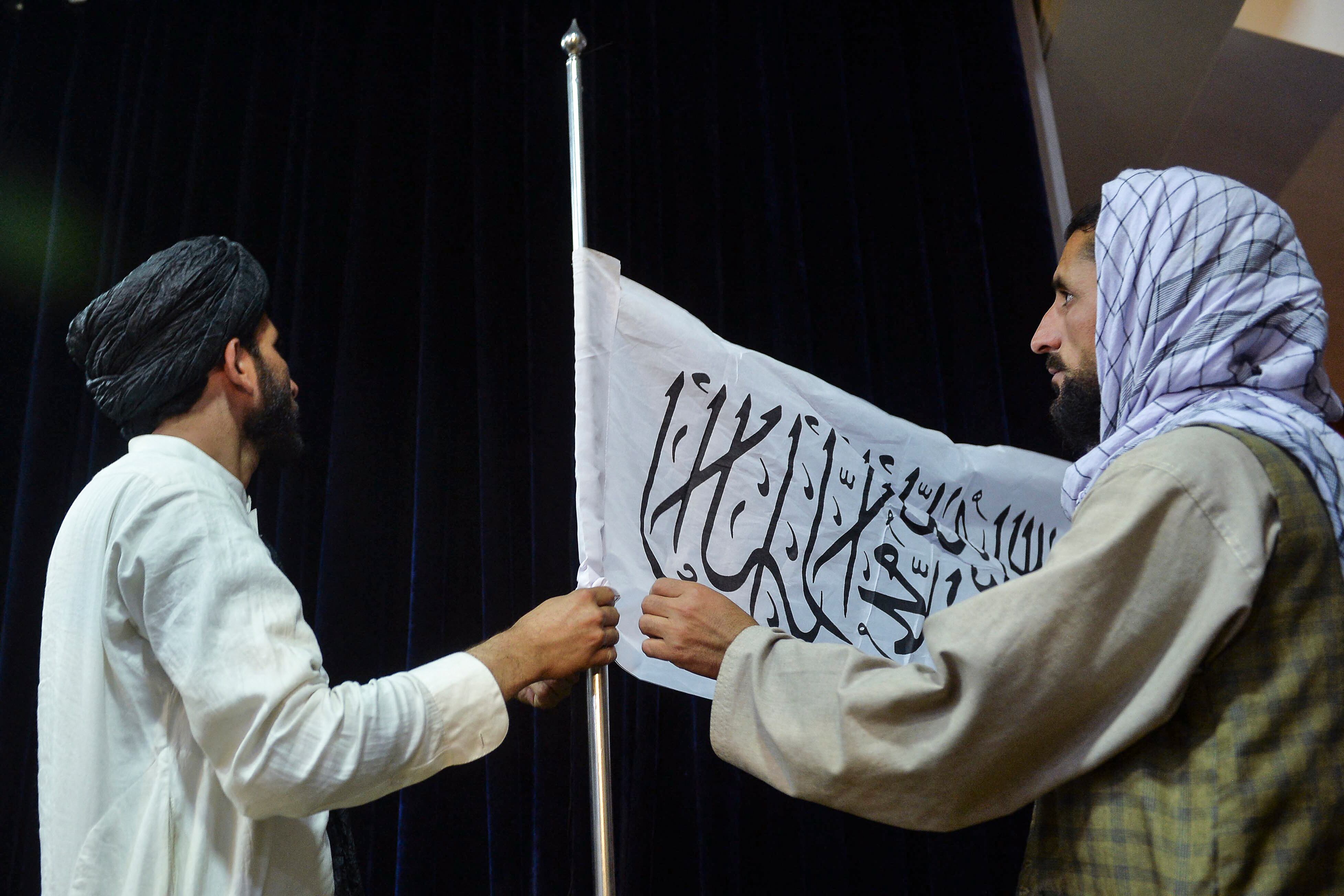 El portavoz talibán Zabihullah Mujahid poniendo una bandera del emirato talibán. (Photo by Hoshang Hashimi / AFP)