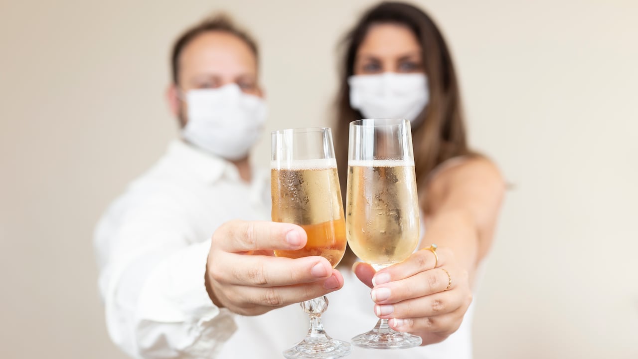 Pareja con tapabocas protectoras celebrando con un vaso para beber.