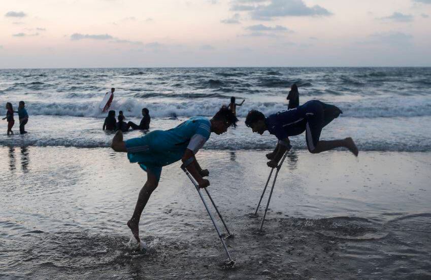 Mohammed Eliwa, de 17 años, y Ahmed al-Khoudari, de 20 años, que perdieron las piernas durante los enfrentamientos en la frontera con Israel, juegan en la playa en la ciudad de Gaza, el 20 de agosto de 2019. (Foto por MAHMUD HAMS / AFP )