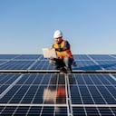 A handyman looking at the laptop on rooftop and testing solar panels.