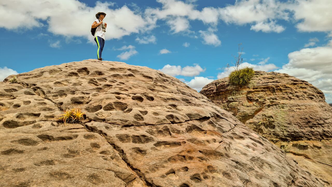 Mujer con mochila en lo alto de una roca sedimentaria mirando al horizonte