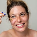 A beautiful woman with freckles applies serum to her face with a pipette