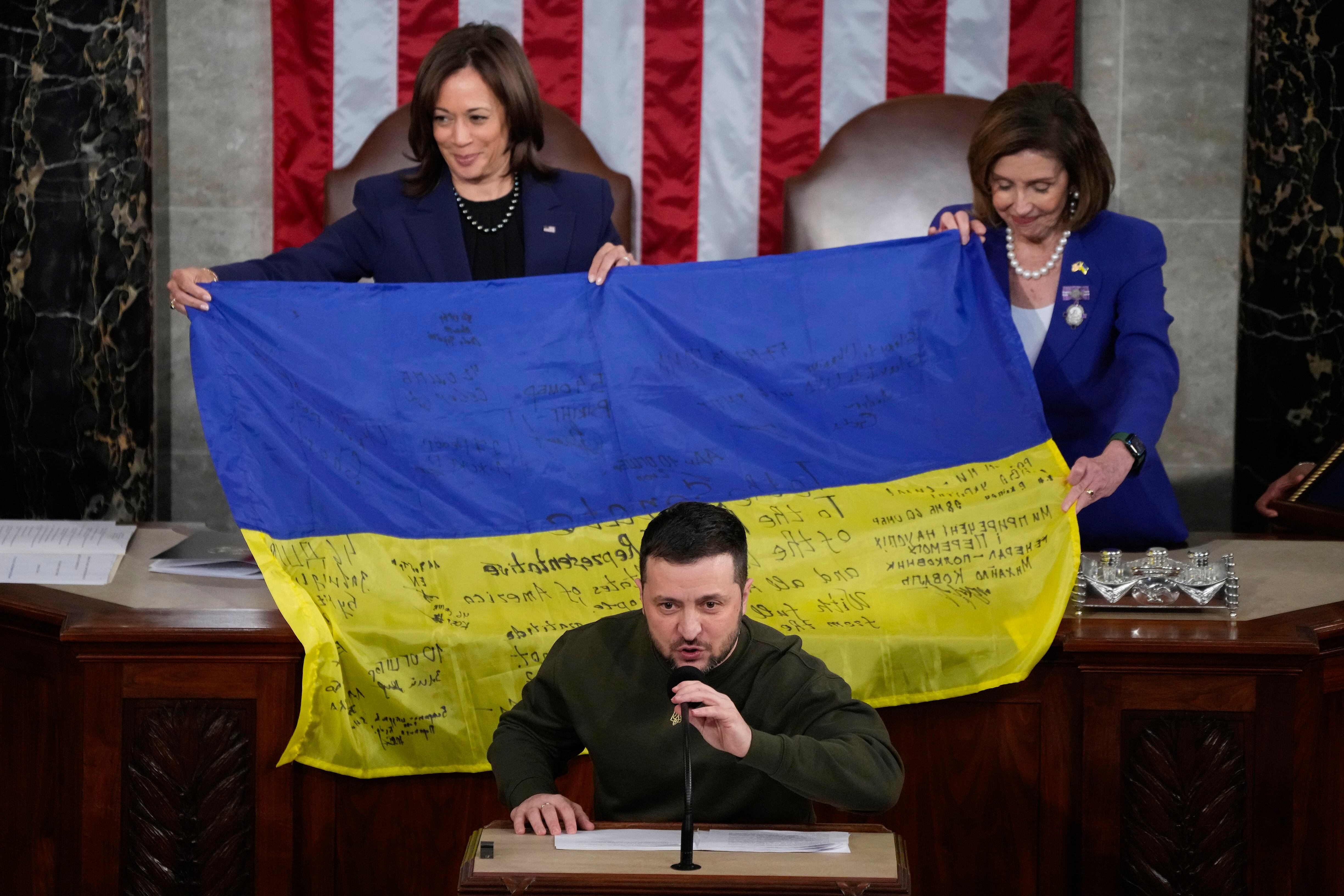 La vicepresidenta Kamala Harris y la entonces presidenta de la Cámara de Representantes, Nancy Pelosi, de California, a la derecha, reaccionan mientras el presidente ucraniano Volodymyr Zelenskyy presenta a los legisladores una bandera ucraniana autografiada por tropas de primera línea en Bakhmut, en la disputada provincia ucraniana de Donetsk, mientras se dirige a un reunión conjunta del Congreso en Capitol Hill el miércoles 21 de diciembre de 2022.