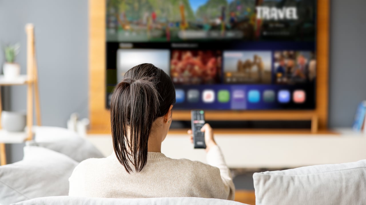 Mujer en casa sosteniendo el control remoto: conceptos de servicios de streaming.