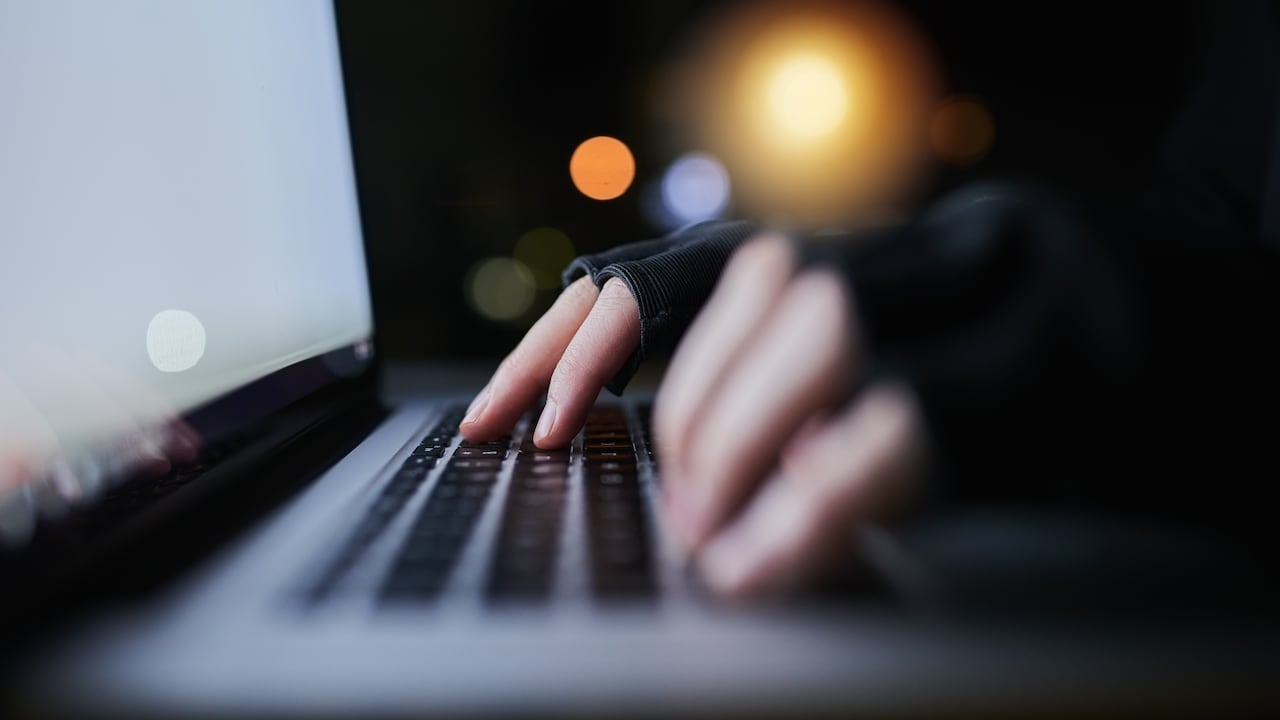 Shot of an unrecognizable computer hacker using a laptop late at night