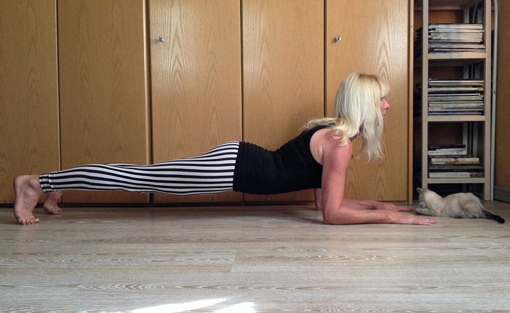 Una mujer en pose de tablón haciendo ejercicio en su dormitorio con un gato mirando