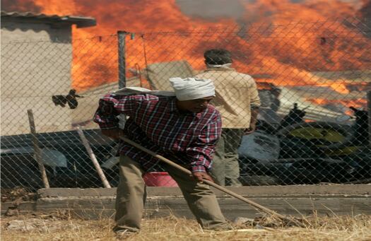 Un hombre despeja la hierba seca delante de su hogar dejada por el fuego producido en el este de Atenas, Grecia.