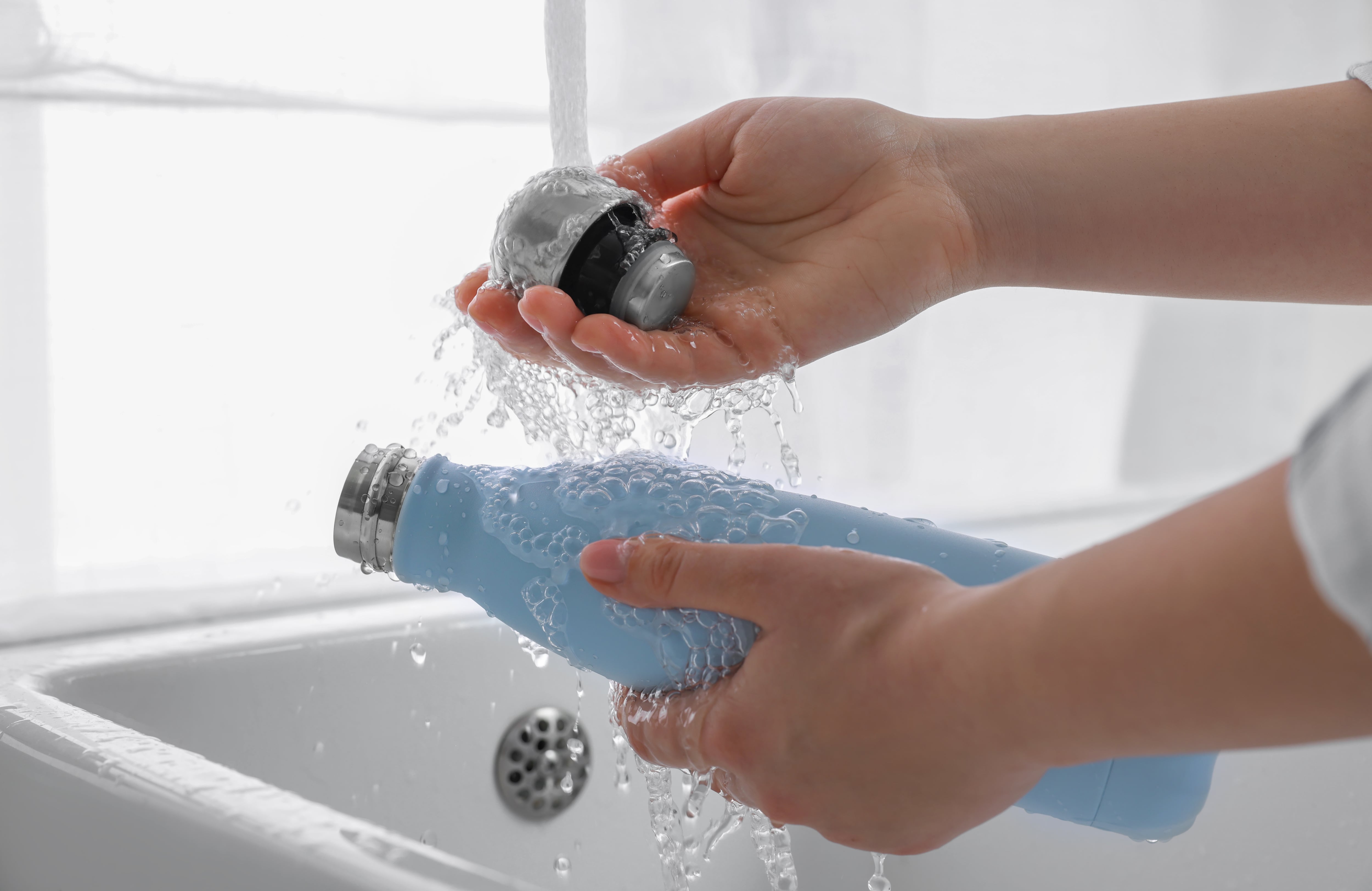 Mujer lavando una botella térmica en la cocina