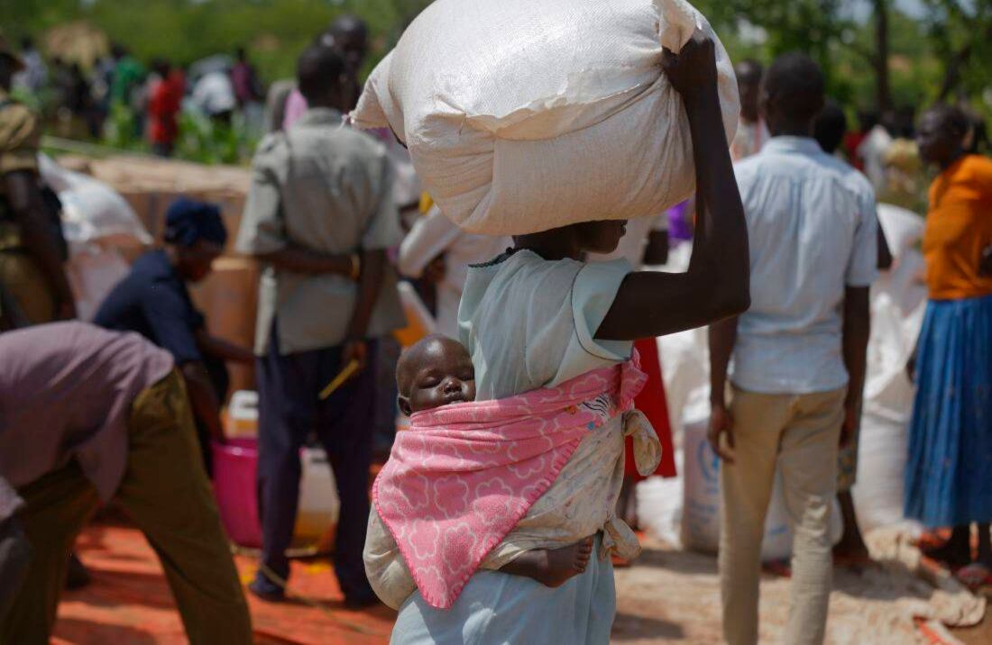 Un bebé sudanés refugiado duerme sobre la espalda de su madre mientras lleva un saco de maíz pesado después de recibir una distribución de alimentos(Foto de AP / Ben Curtis)  