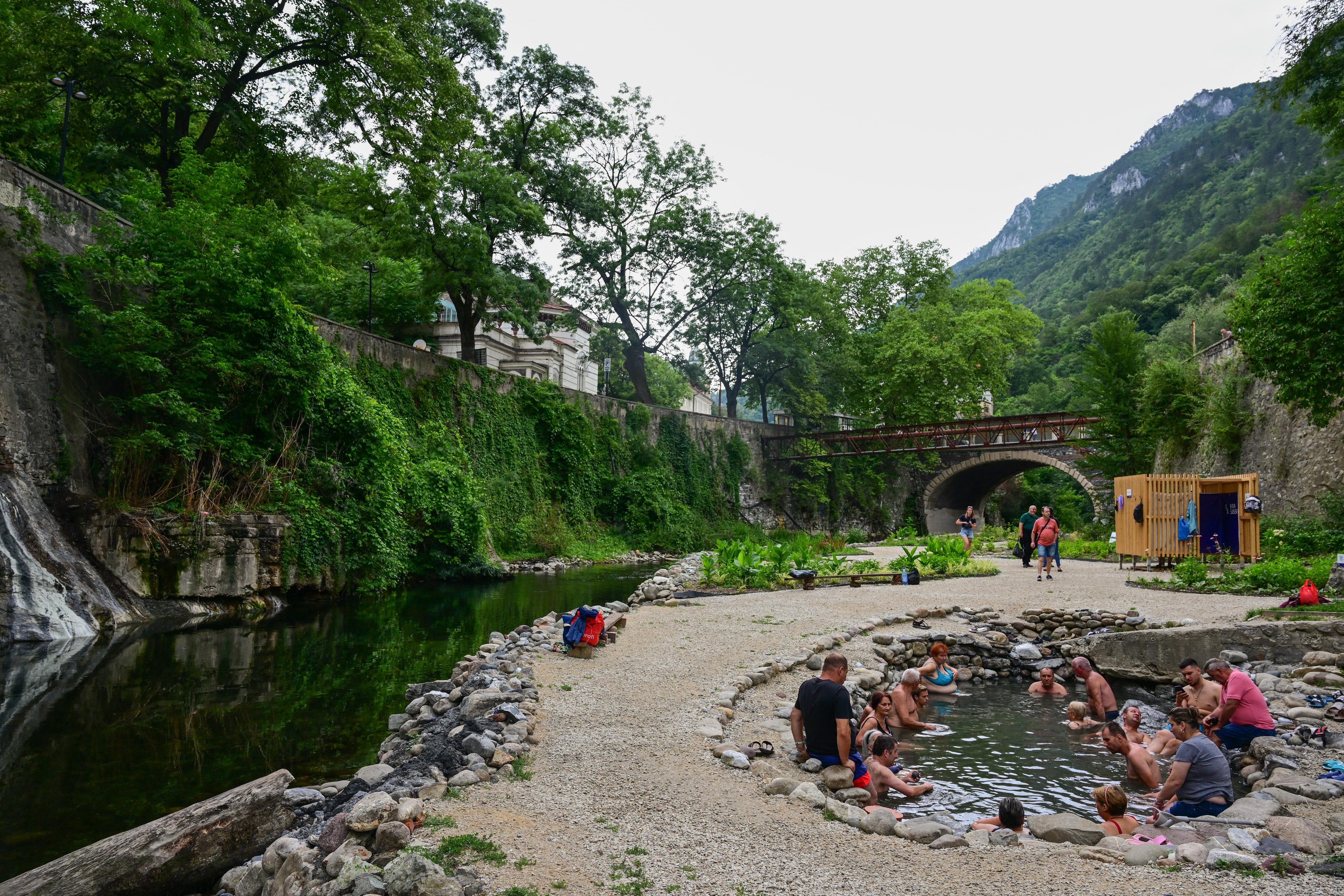 Los turistas disfrutan de aguas termales sulfurosas en piscinas ajardinadas restauradas por un grupo de jóvenes arquitectos liderados por Oana Chirila, junto al lecho del río Cerna en Baile Herculane el 29 de julio de 2025. Con grafitis que cubren las paredes desmoronadas de los principales baños termales en una de las ciudades balneario más antiguas de Europa, un grupo de jóvenes arquitectos espera restaurar el pintoresco balneario rumano que una vez atrajo a emperadores después de décadas de abandono y corrupción. Foto Daniel MIHAILESCU / AFP