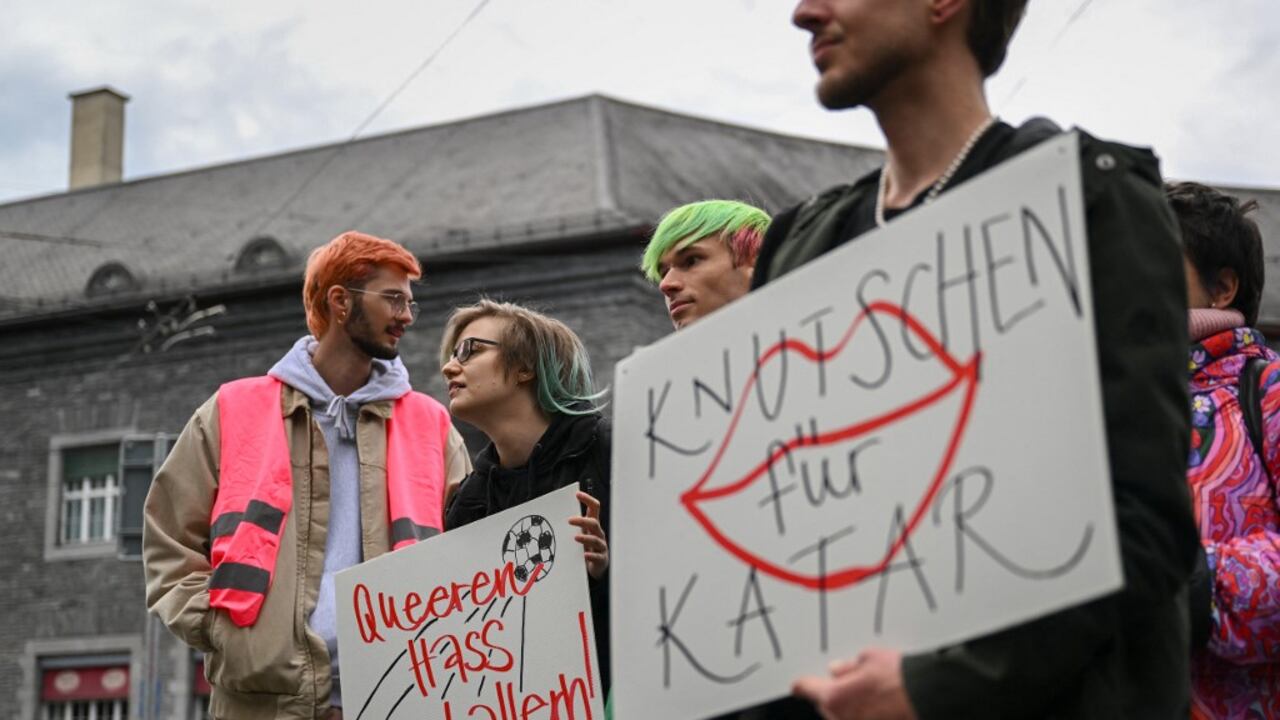 Activistas sostienen carteles que dicen en alemán "disparando al odio queer" y "Besándose por Qatar" durante una acción simbólica de asociaciones LGBT+ frente al museo de la FIFA en Zúrich el 8 de noviembre de 2022, para llamar a la FIFA a defender los derechos de la comunidad LGBT+ antes del torneo de fútbol de la Copa Mundial de la FIFA Qatar 2022 que comenzará el 20 de noviembre. (Foto de Fabrice COFFRINI / AFP)