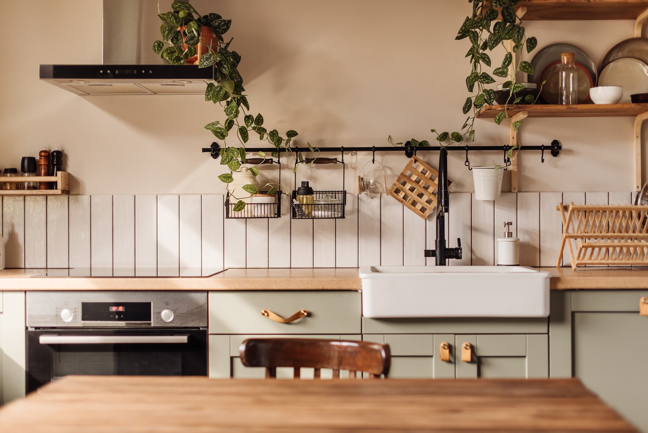 Empty kitchen island with marble surface in foreground, green vintage countertop with drawers and pendant lights hanging above, lots of flowers in jars, blurred background