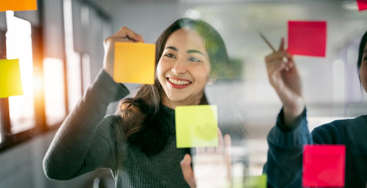 Young businesswoman creative team using post it notes in glass wall to writing strategy business plan to development grow to success.
