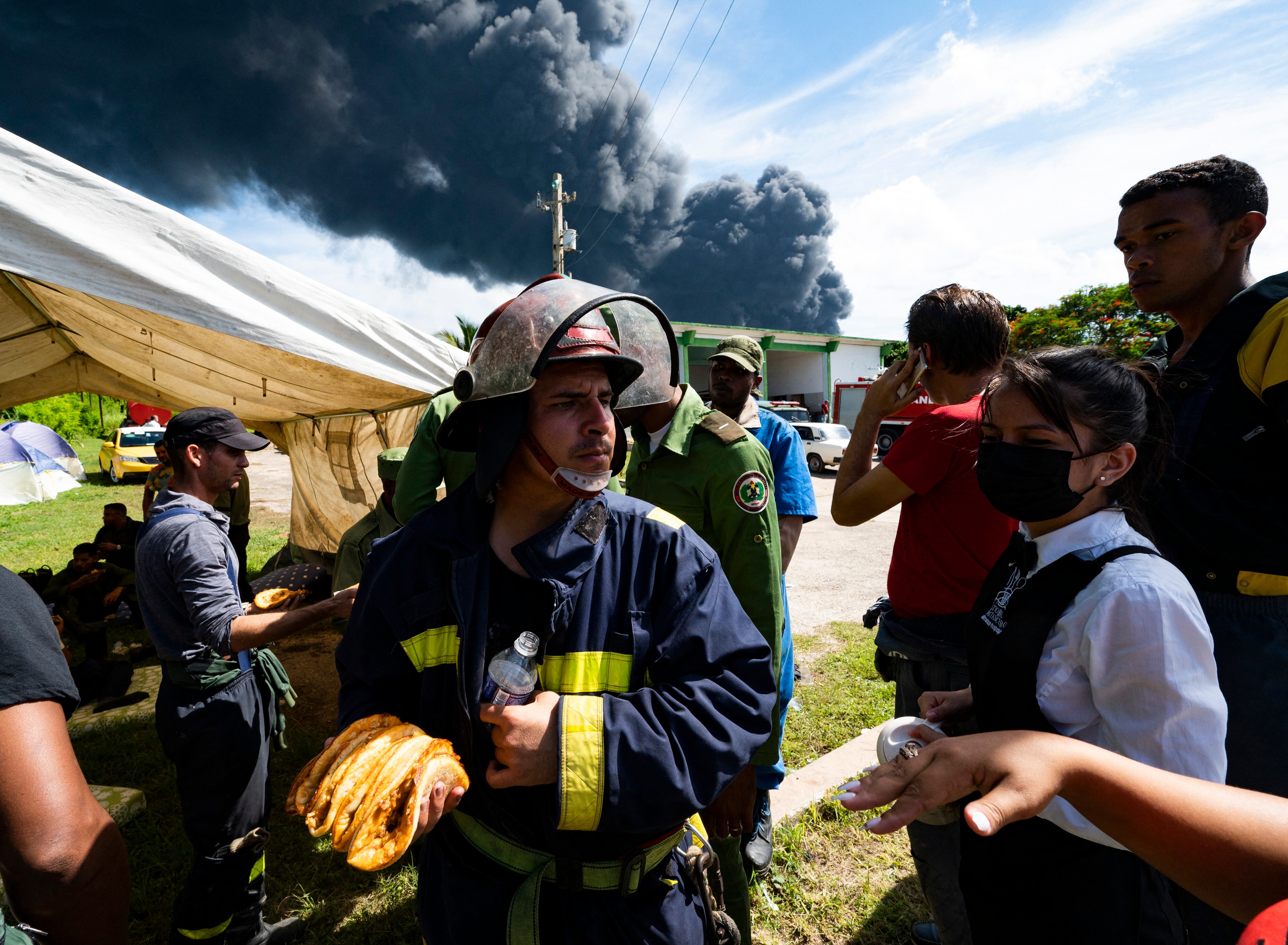 Los bomberos reciben alimentos después de trabajar en el incendio masivo en un depósito de combustible provocado por un rayo en Matanzas, Cuba, el 8 de agosto de 2022. - Helicópteros del ejército cubano se apresuraron a contener un incendio que derribó un tercer tanque en un depósito de combustible el lunes después de ardiendo durante días, mientras continuaba la búsqueda de 16 bomberos desaparecidos. (Foto de YAMIL LAGE / AFP)