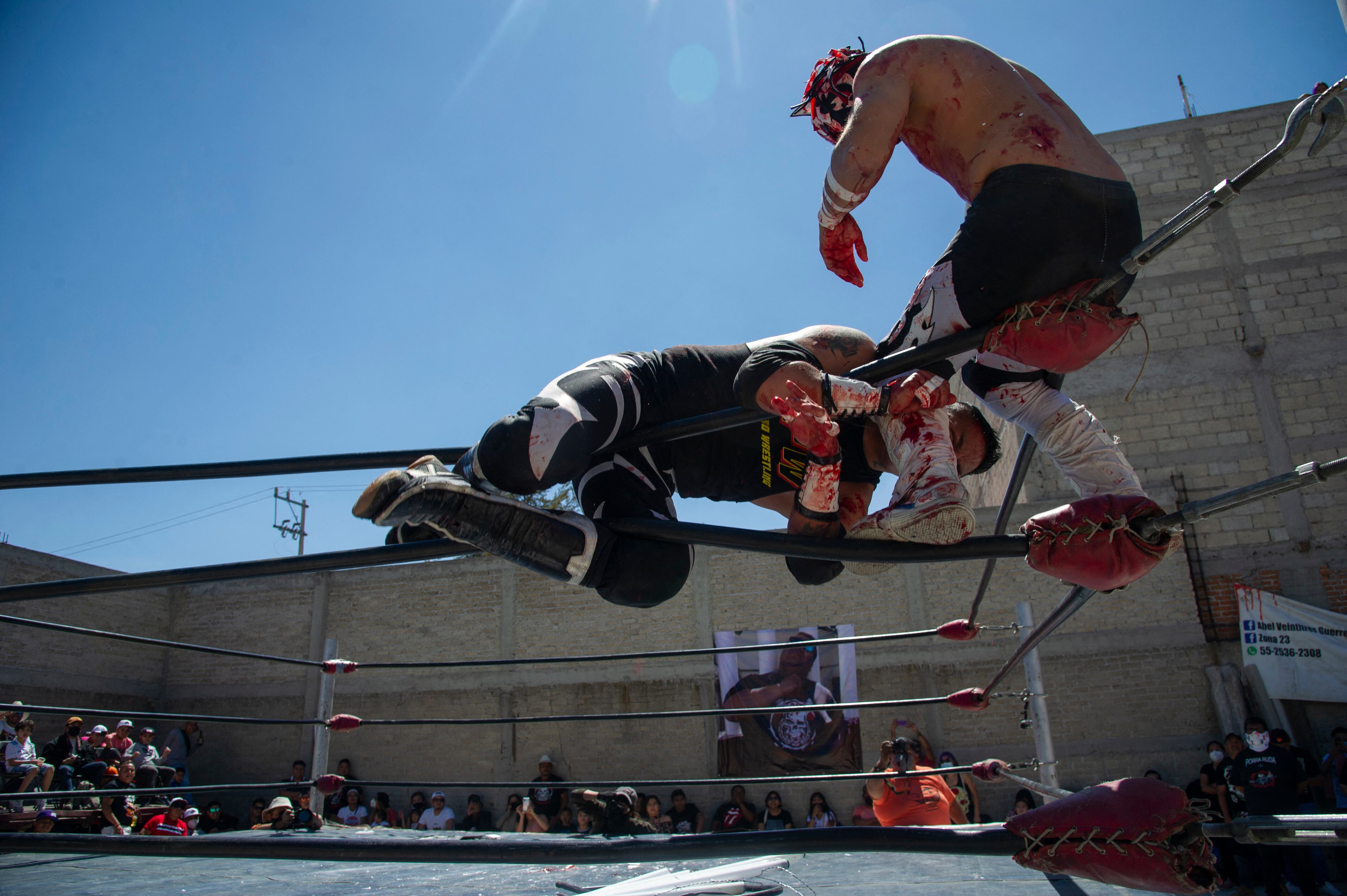Mexican wrestlers take part in the clandestine backyard show Hall of Fame, mounted by extreme wrestling organizer Zona 23, which pays tribute to wrestler Israel Montiel Leon, "Ovett", who died of COVID-19 in February this year at the age of 44, and two other fighters, in Cuautitlan Izcalli, Mexico State, Mexico, on April 4, 2021. - Almost 200 Mexican extreme wrestlers have died from COVID-19, their worst contender. (Photo by Claudio CRUZ / AFP)