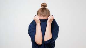 Mujer europea escondiendo la cara debajo de la ropa. Ella está tirando suéter en su cabeza. Emoción deprimida. Deseo estar solo.