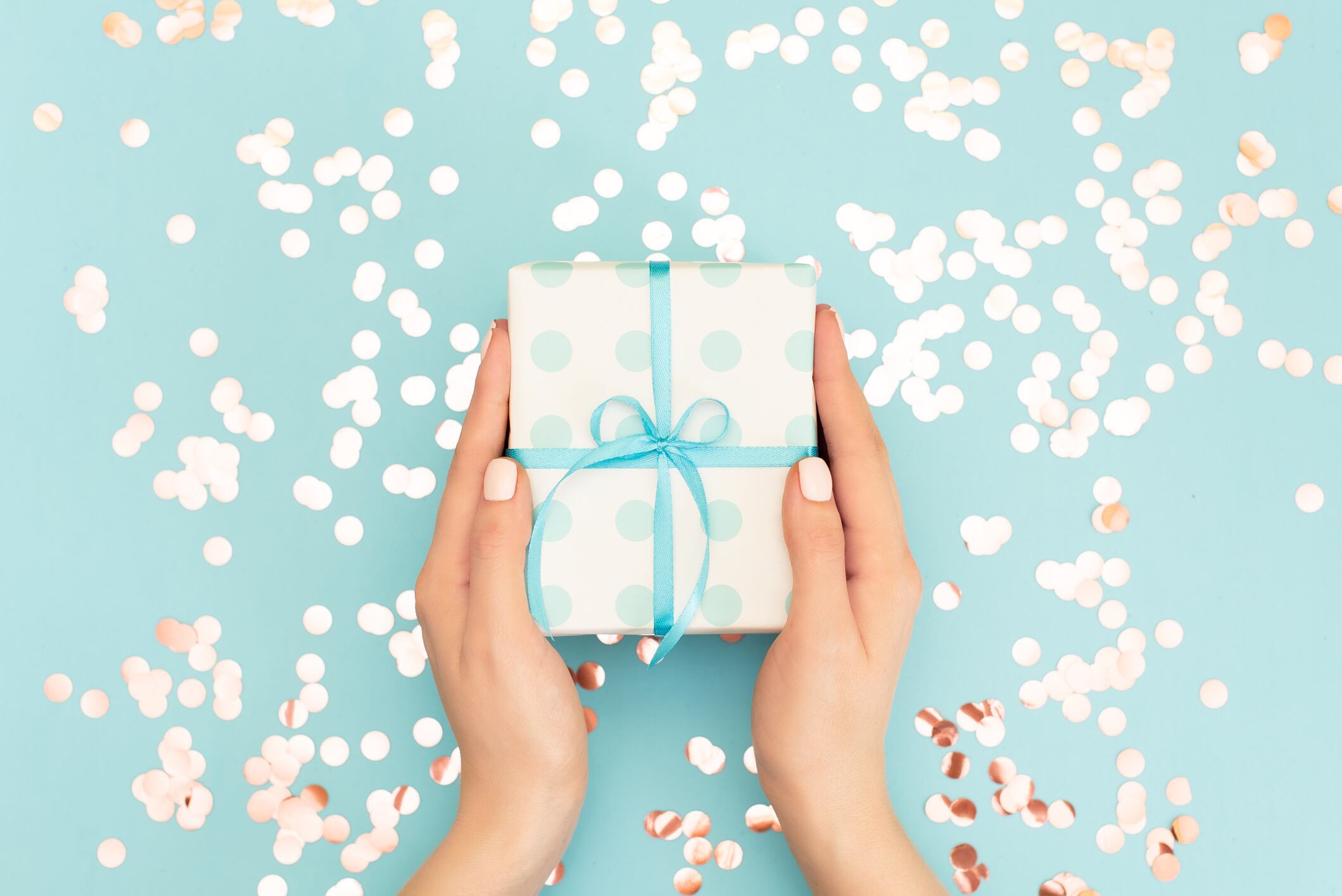 Womans hands holding gift or present box decorated confetti on pink pastel table top view. Flat lay composition for birthday or wedding