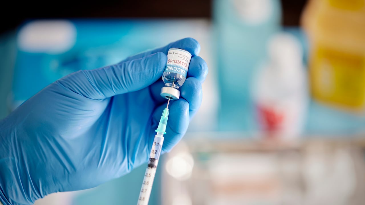 Un trabajador de la salud pone guantes quirúrgicos y saca el líquido de la vacuna COVID-19 del vial para vacunar a un paciente