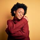 Joven y hermosa mujer afroamericana afro con el pelo rizado y un suéter casual de cuello alto Abrazándose feliz y positiva, sonriendo confiada. Amor propio y cuidado propio