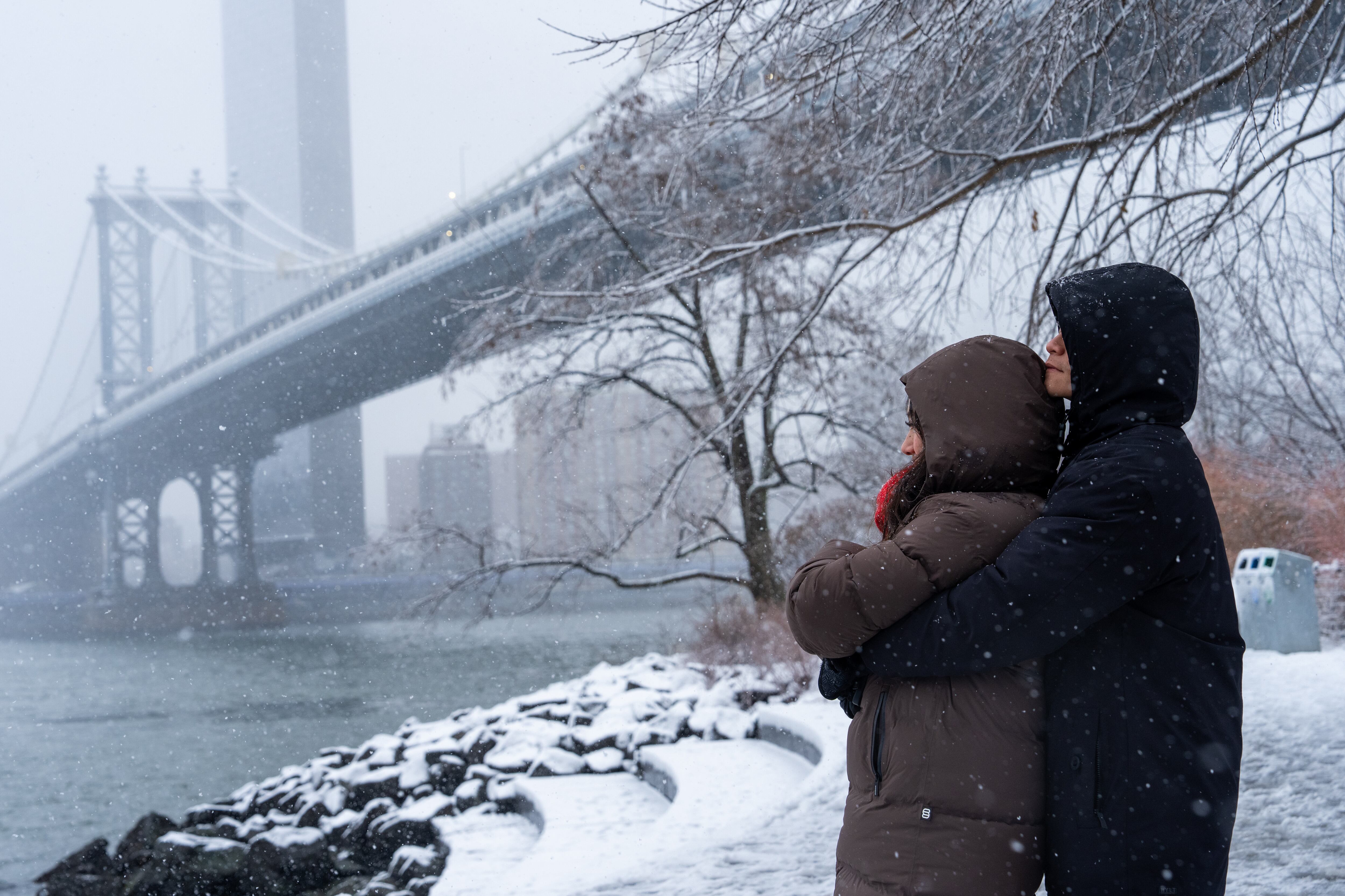 Una pareja se abraza durante la nieve frente al puente de Manhattan, el domingo 14 de diciembre de 2025, en el distrito de Brooklyn de Nueva York