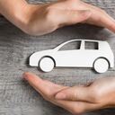 Manos protegiendo el icono del coche sobre la mesa de madera. Vista superior de las manos que muestran el gesto de proteger el coche. Seguro de automóvil y concepto de negocio automotriz.