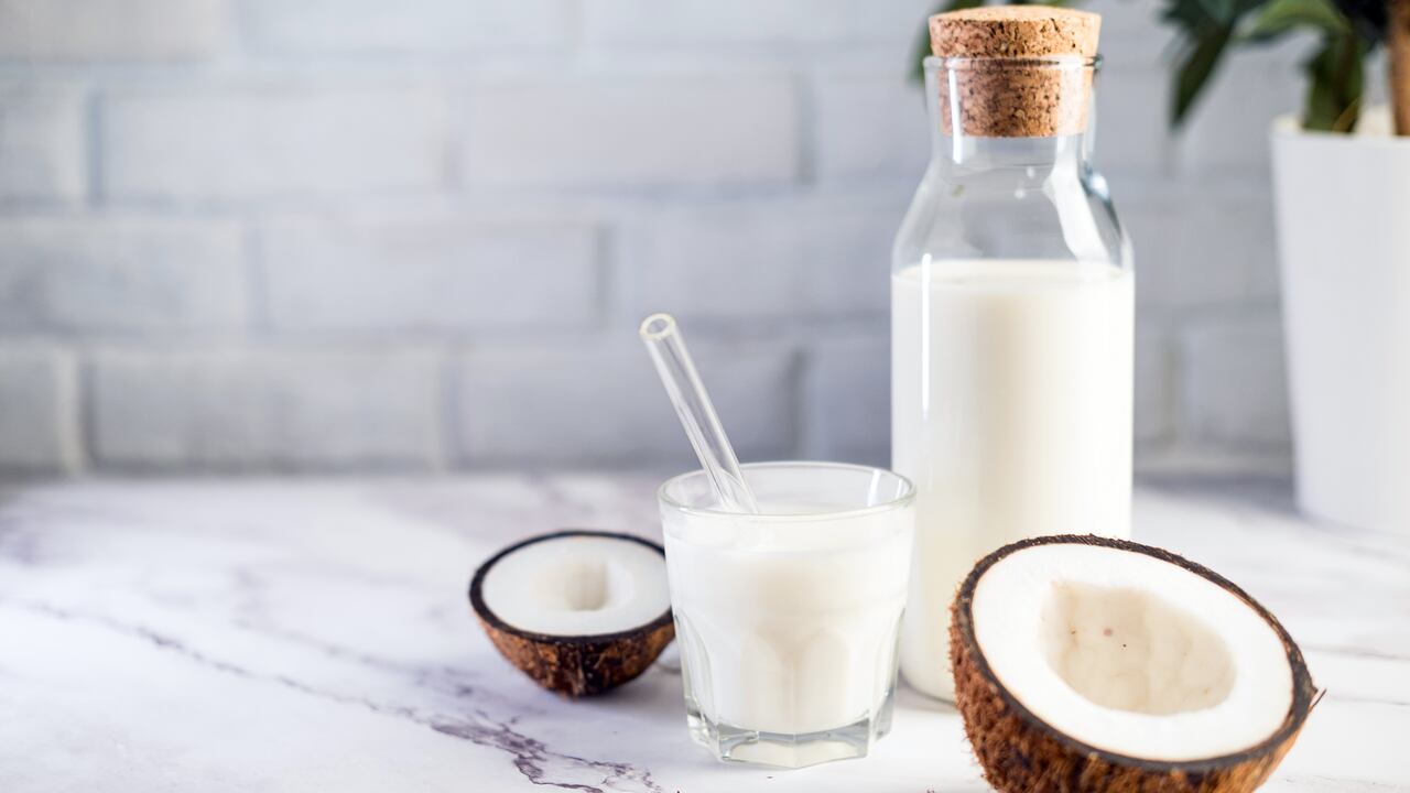 Glass bottle with milk on white kitchen table with coconut aside. Vegan non dairy healthy or fermented drink. Healthy eating concept.