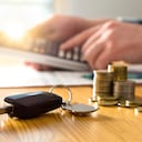 Car keys and money on table with man using calculator. Buyer counting savings and gas cost or salesman calculating sales price, vehicle value or road taxes.