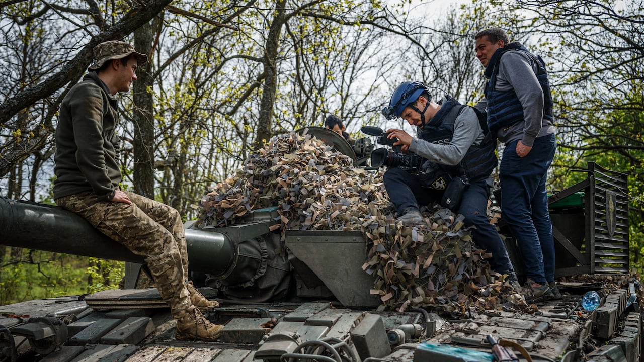 El periodista visual de la AFP Arman Soldin (2do der.) se sienta en un tanque militar ucraniano durante una entrevista con un soldado, junto con el reparador Oleksiy Obolensky (der) en la región de Donbass el 29 de abril de 2022.
