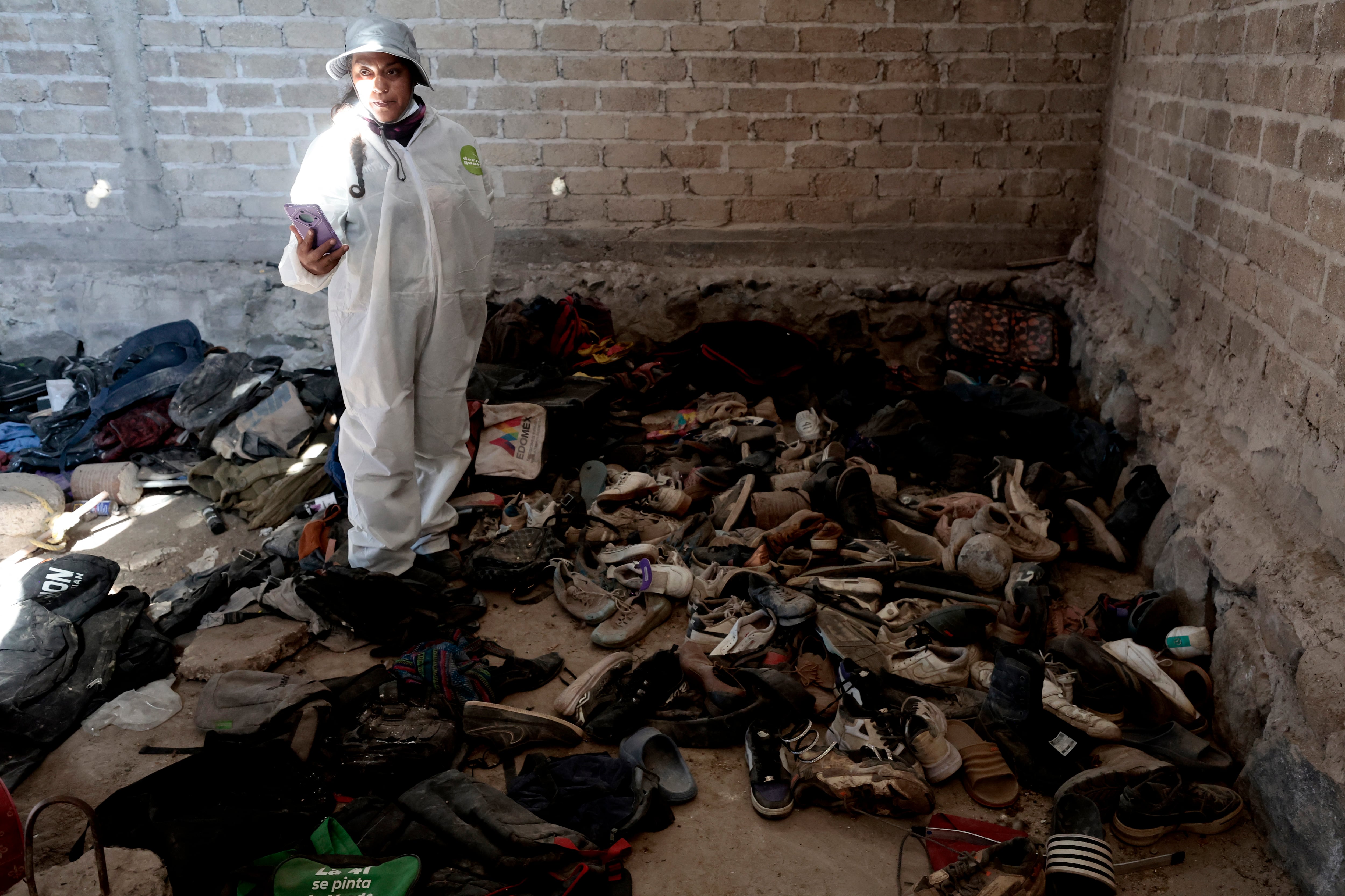 Una mujer registra ropa y zapatos encontrados en el Rancho Izaguirre, en la comunidad de La Estanzuela, donde el colectivo "Guerreros Buscadores" localizó tres crematorios humanos mientras buscaba a sus familiares en Teuchitlán, Jalisco, México, el 5 de marzo de 2025.