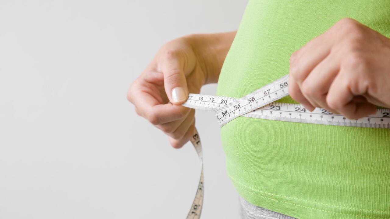 Fat overweight woman measuring her waist. Plus size. New start for healthy lifestyle, body slimming and weight loss. Care about body. Copy space. Empty place for text on gray background.