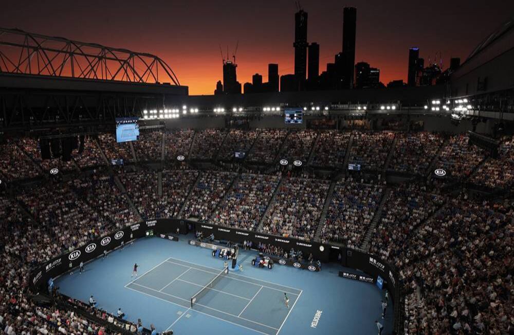 En el Rod Laver Arena, Roger Federer (Suiza) y Novak Djokovic (Serbia) juegan su partido de semifinal, mientras se pone el sol, de tonos rojizos y amarillos, en el campeonato de tenis Open de Australia en Melbourne, el jueves 30 de enero de 2020. Foto: Andy Wong/ AP.