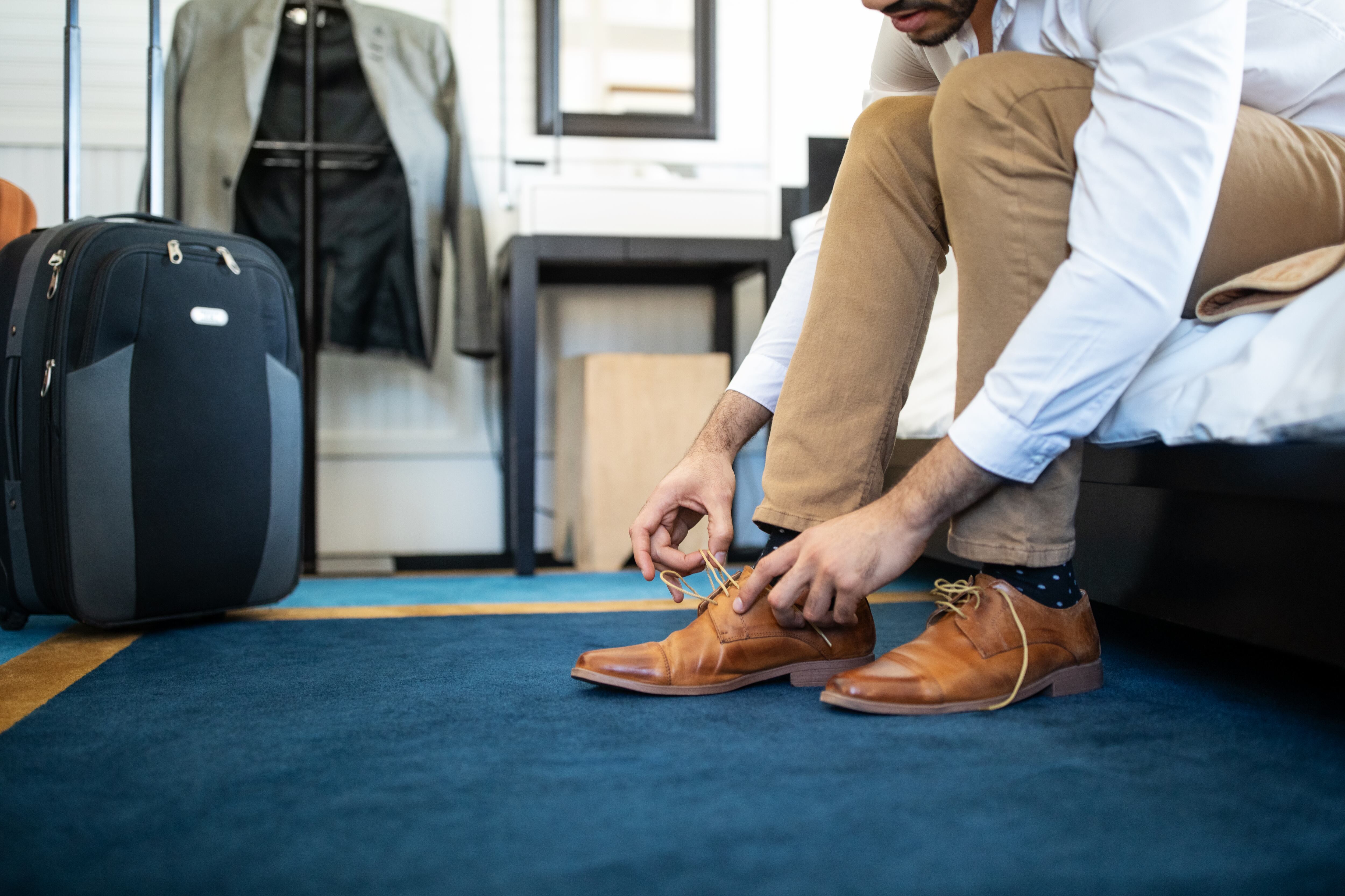 Cropped shot of man removing his shoe sitting on hotel bed. Businessman takes off his shoe in hotel room.