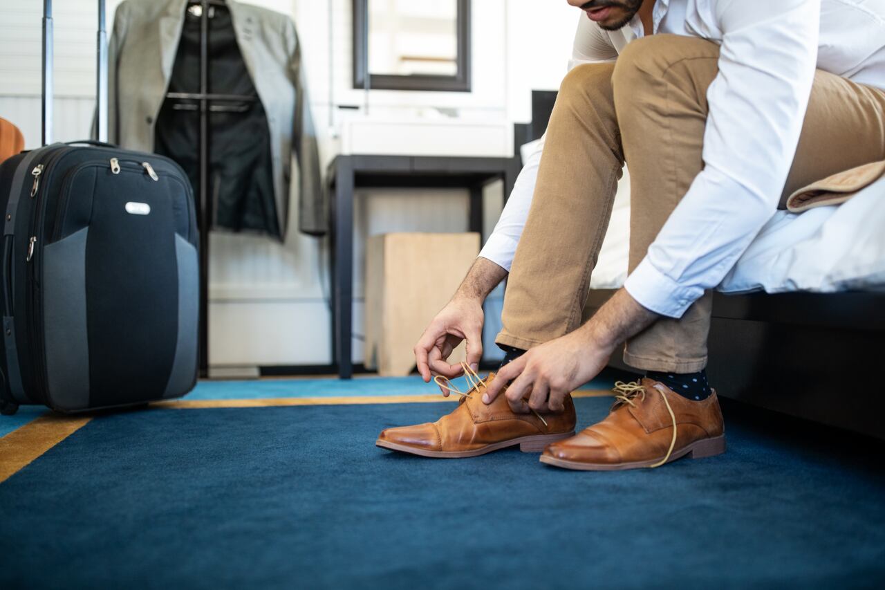 Cropped shot of man removing his shoe sitting on hotel bed. Businessman takes off his shoe in hotel room.