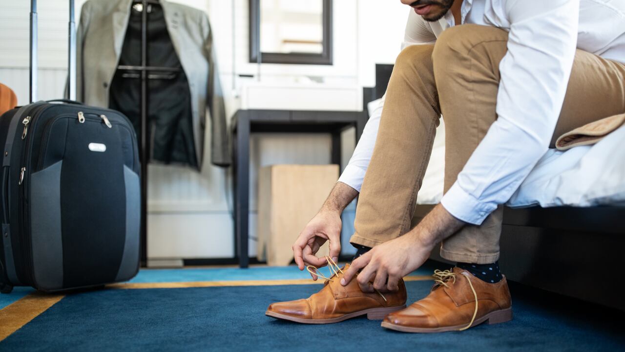 Cropped shot of man removing his shoe sitting on hotel bed. Businessman takes off his shoe in hotel room.