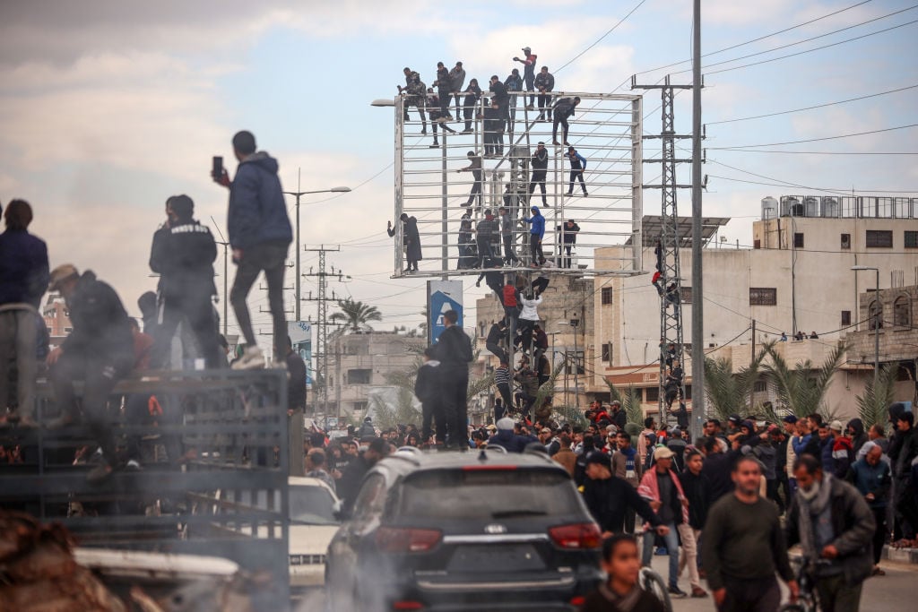 Palestinians gather beside a street and some climb up on a billboard stand to watch Hamas fighters hand over three Israeli hostages to a Red Cross team in Deir el-Balah, central Gaza, on February 8, 2025. Hamas militants hand over three Israeli hostages on February 8, as part of the fifth exchange under a fragile Gaza ceasefire, with 183 prisoners held by Israel due to be released later in the day. (Photo by Majdi Fathi/NurPhoto via Getty Images)