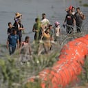 Migrantes en su ruta hacia Estados Unidos desde México se acercan al punto en el que trabajadores están instalando grandes boyas a modo de barrera flotante sobre el río Bravo, en Eagle Pass, Texas, el martes 11 de julio de 2023. La barrera flotante se dispuso en un intento de bloquear el paso a Texas desde México.