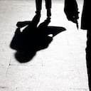 Blurry silhouette and shadow of a woman carrying a bag and a man holding sharp object following her, in the city street in the night